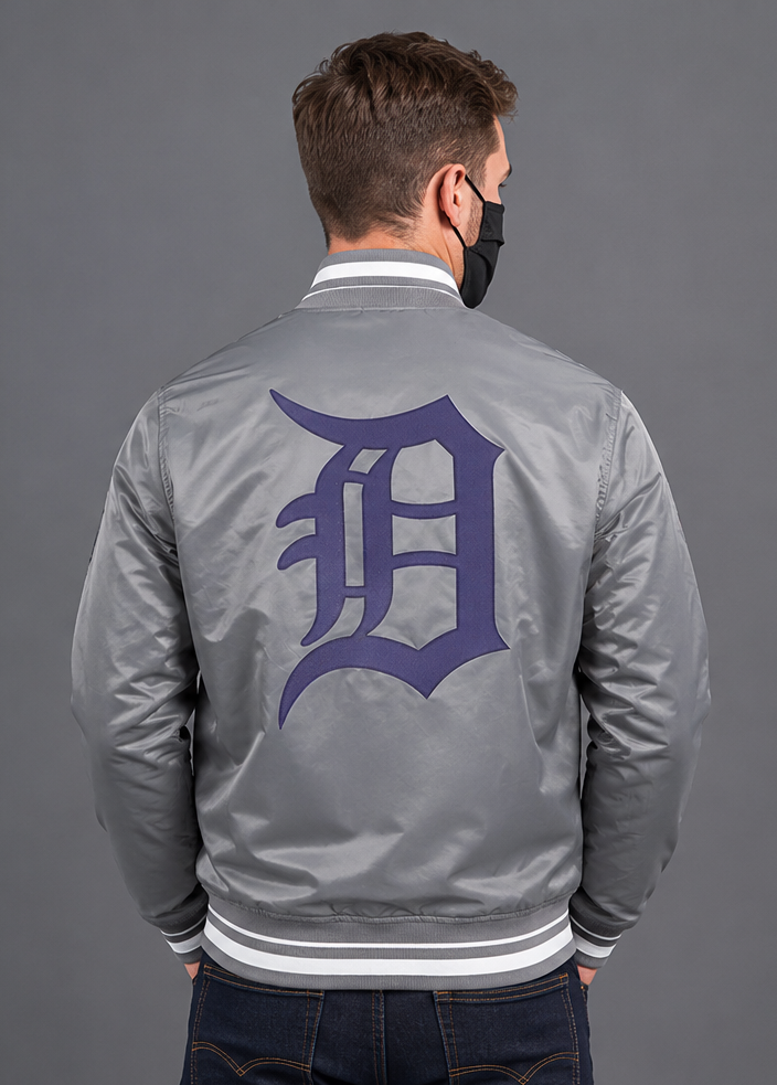 A man viewed from behind wearing a gray satin letterman jacket with a large purple 'D' logo on the back, white ribbed collar and hem, and a black face mask.