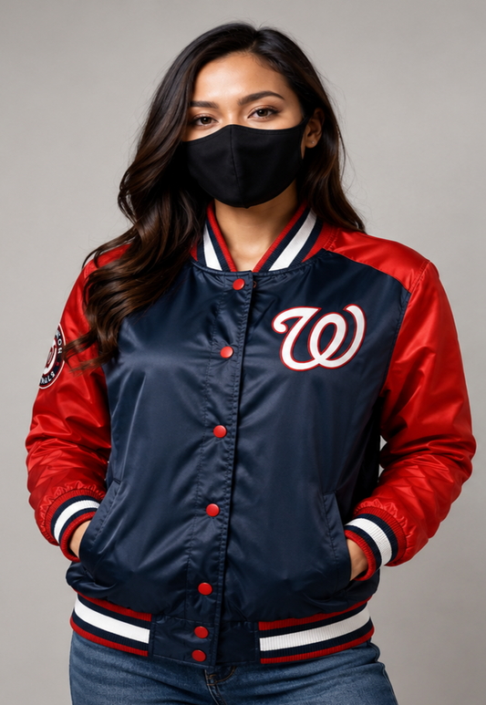 A woman wearing a navy and red satin varsity jacket with the Washington Nationals 'W' logo on the chest, paired with a black face mask and blue jeans, against a neutral gray background.