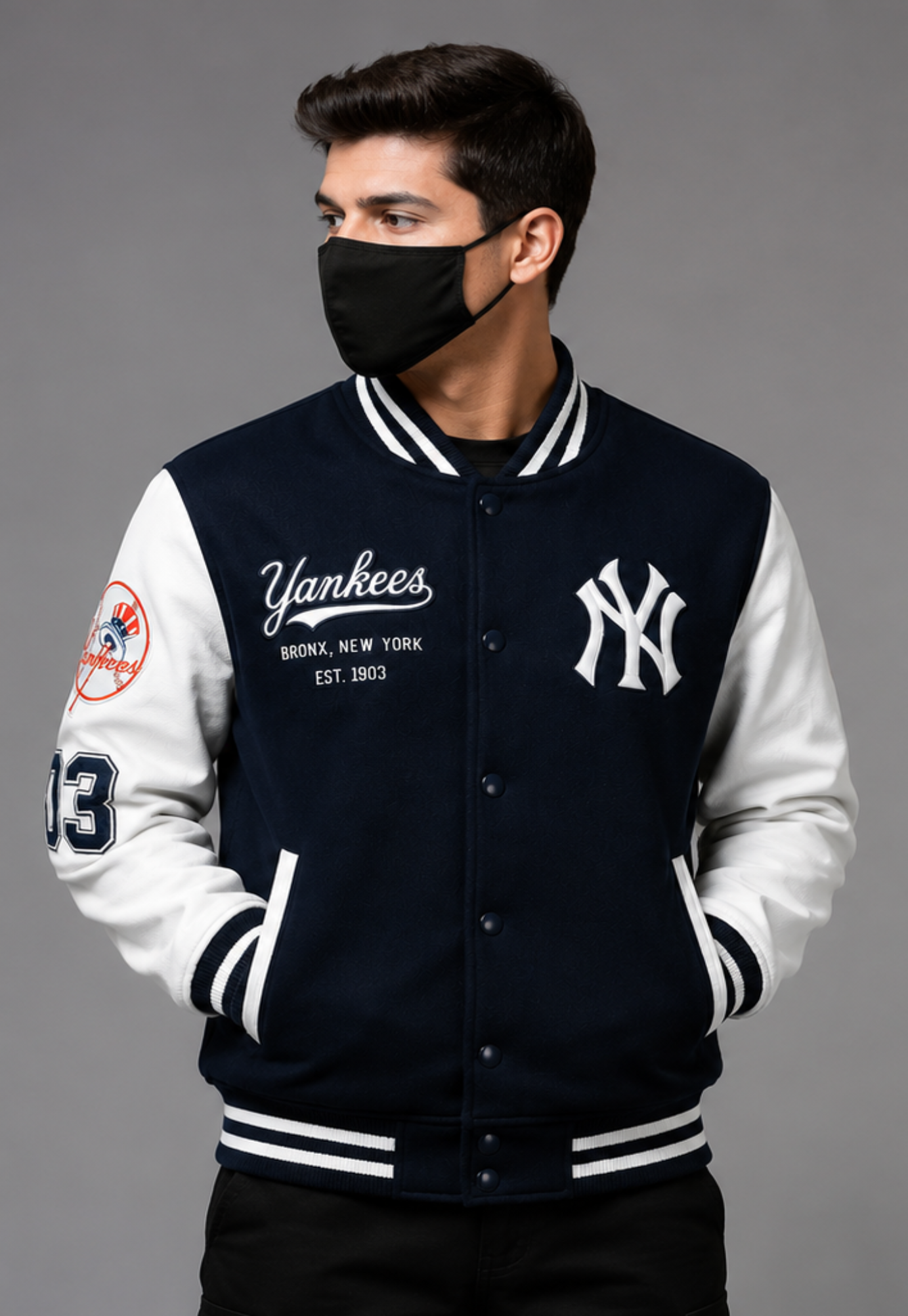 A man wearing a navy and white New York Yankees varsity jacket, featuring the Yankees logo on the chest and 'Yankees' script on the front, posed against a solid gray background.