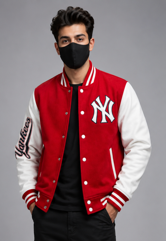 A man wearing a red and white New York Yankees varsity jacket over a black shirt and black pants, standing against a gray studio background.