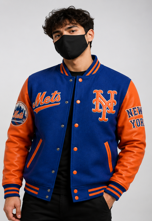 A man wearing a blue and orange New York Mets varsity jacket, featuring orange leather sleeves and a royal blue fleece body with orange lettering, including 'Mets' on the chest and 'NEW YORK' on the sleeve.