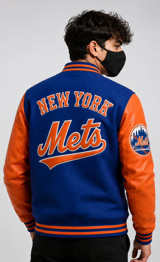 A man wearing a blue and orange New York Mets varsity jacket, shown from the back. The jacket features blue wool body with orange leather sleeves and 'NEW YORK Mets' lettering on the back.