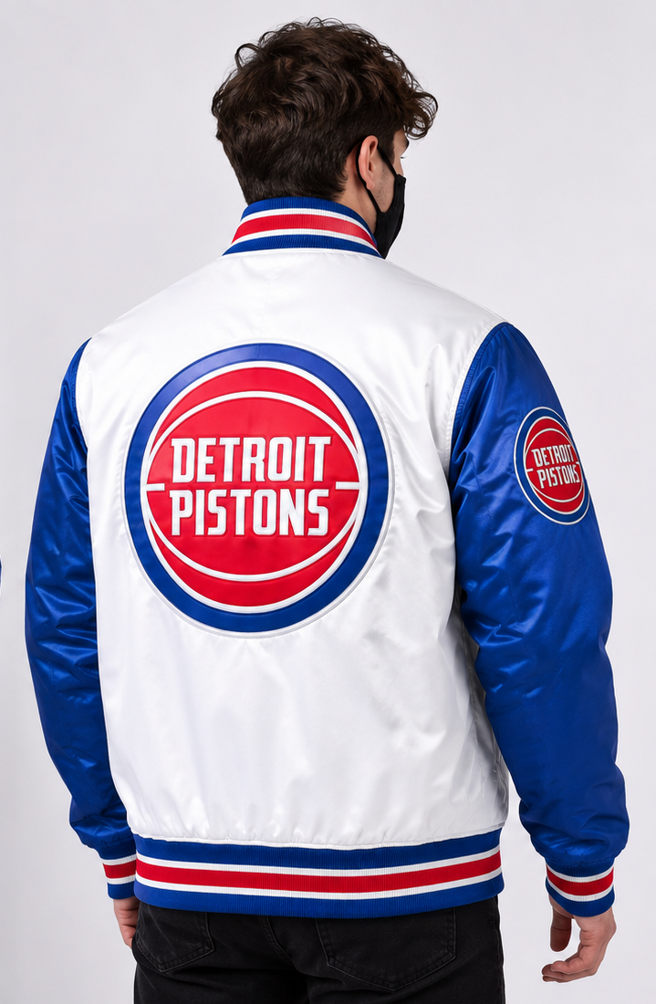 A man viewed from the back wearing a Detroit Pistons satin bomber jacket. The jacket features a white body, royal blue sleeves, and red and white striped ribbed trim, with a large circular Detroit Pistons logo patch on the back and a smaller one on the sleeve.