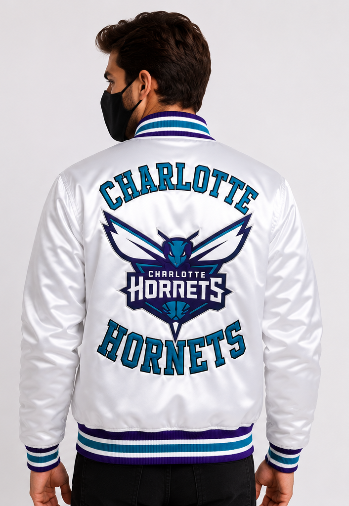 A man wearing a white satin varsity jacket with a large Charlotte Hornets graphic on the back, shown from behind against a light gray studio background.