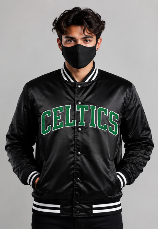 A man wearing a black satin varsity jacket with 'CELTICS' in green and white collegiate block letters across the chest, paired with a black face mask, against a solid gray studio background.