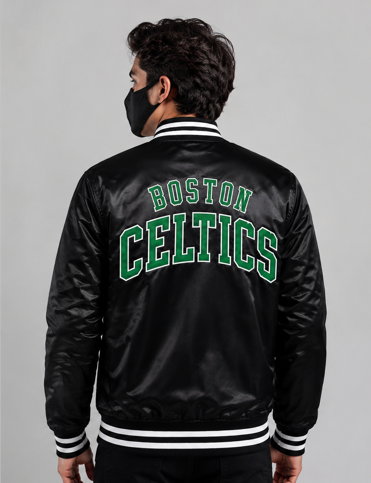 A man viewed from the back wearing a black satin Boston Celtics varsity jacket with green and white lettering on the back, set against a plain gray studio background.