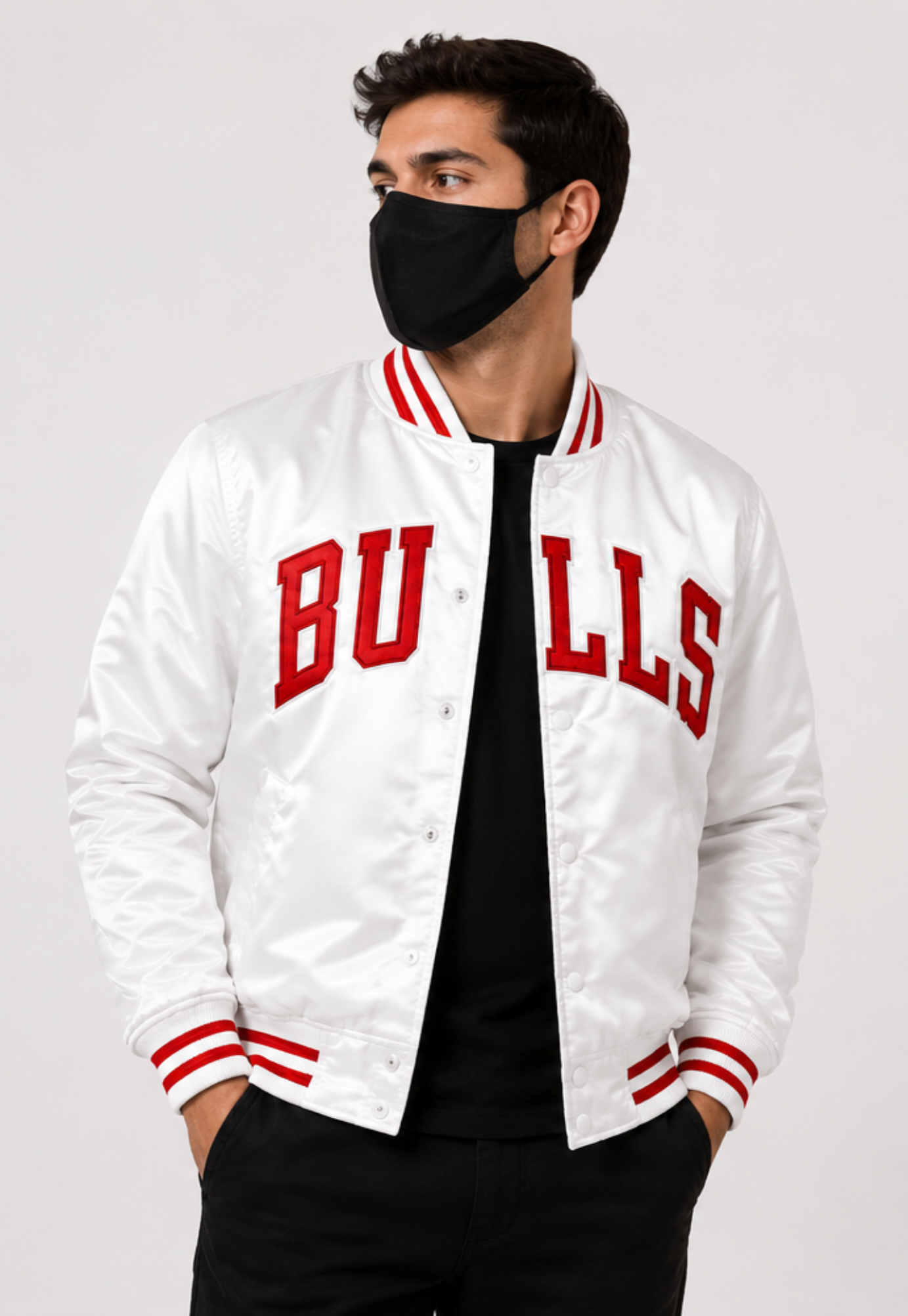 A man wearing a white satin varsity jacket with red 'BULLS' lettering on the front, paired with a black shirt, black pants, and a black face mask, against a light gray studio background.