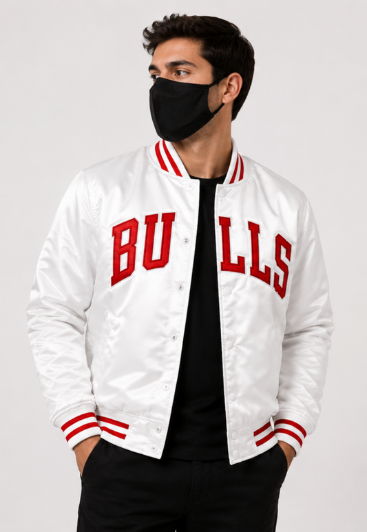 A man wearing a white satin varsity jacket with red 'BULLS' lettering on the front, paired with a black shirt, black pants, and a black face mask, against a light gray studio background.