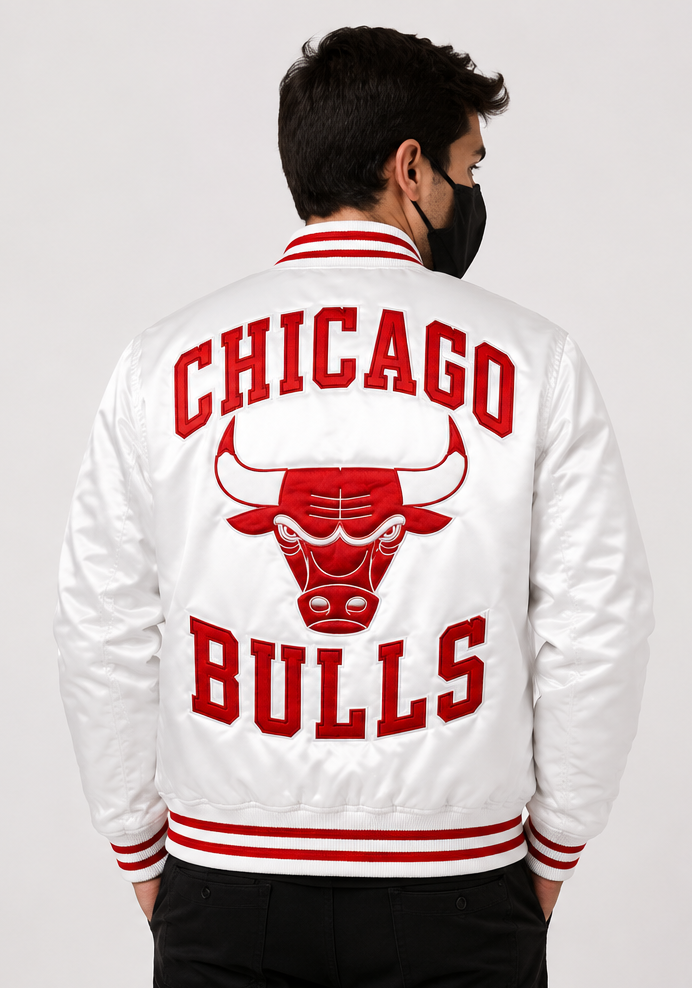 A man viewed from the back wearing a white Chicago Bulls varsity jacket with red lettering and stripes, paired with a black face mask and black pants, against a light gray studio background.