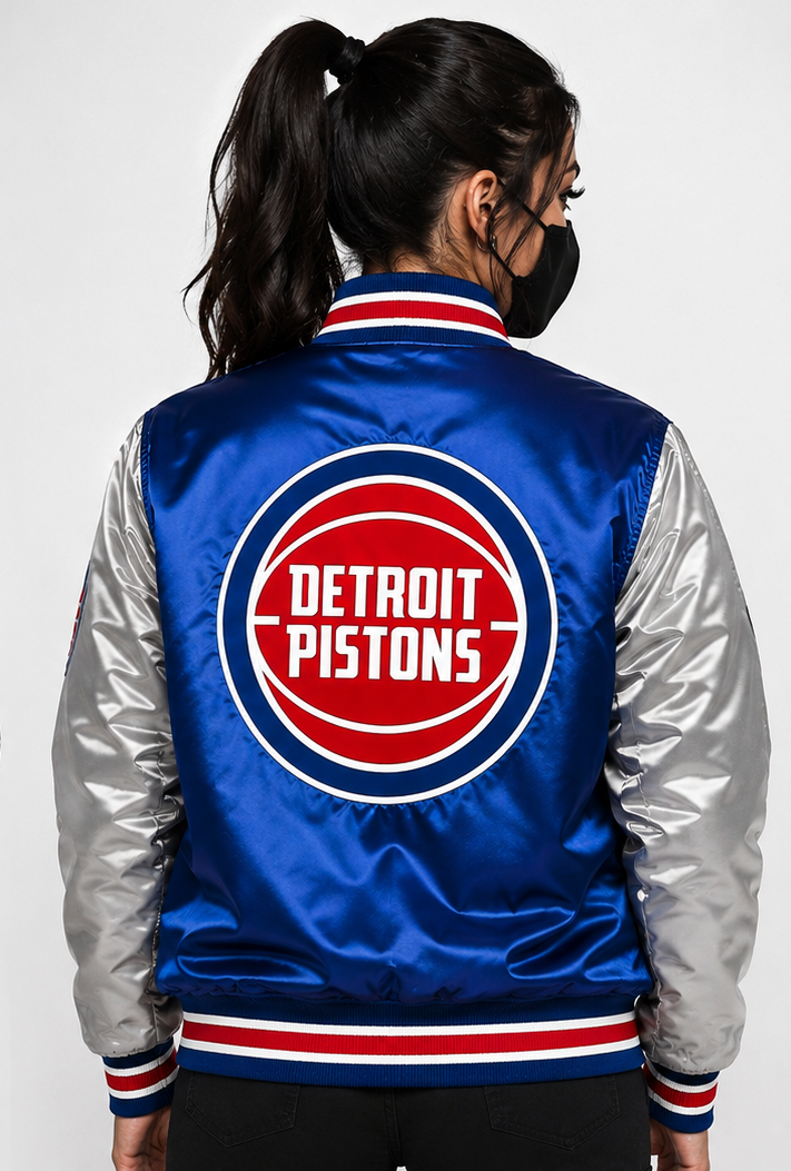 A woman viewed from the back wearing a Detroit Pistons satin bomber jacket with a blue body, silver sleeves, and a large red, white, and blue team logo on the back.