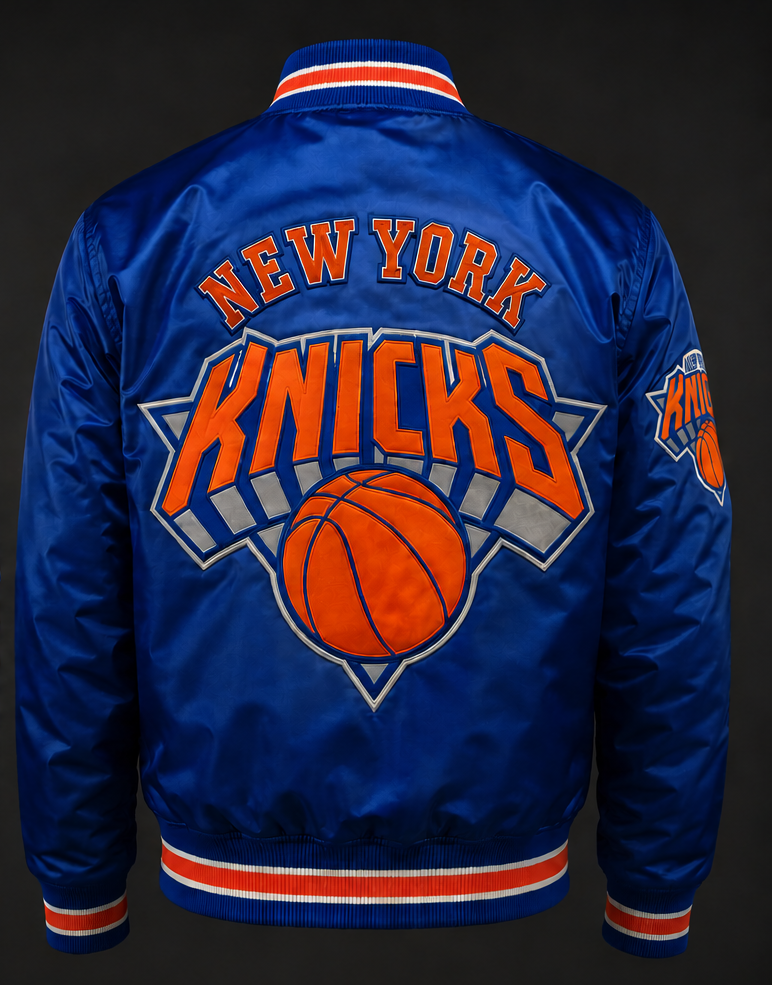 A royal blue satin New York Knicks bomber jacket shown from the back, featuring a large orange and white 'NEW YORK KNICKS' logo with a basketball graphic on the back and a smaller logo on the sleeve.