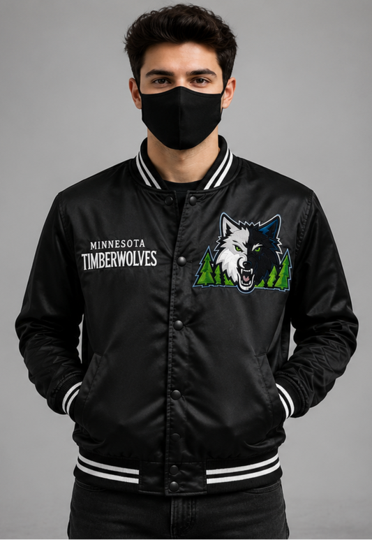 A man wearing a black satin Minnesota Timberwolves varsity jacket with white striped ribbed collar, cuffs, and hem, along with a black face mask, photographed against a neutral gray studio background.