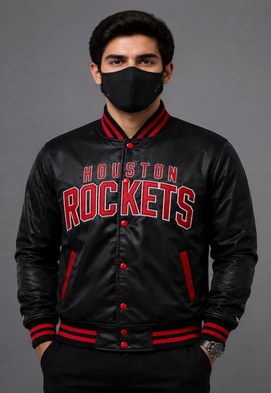 A man wearing a black satin bomber jacket with 'HOUSTON ROCKETS' in red and white lettering on the front, paired with a black face mask, set against a solid gray studio background.
