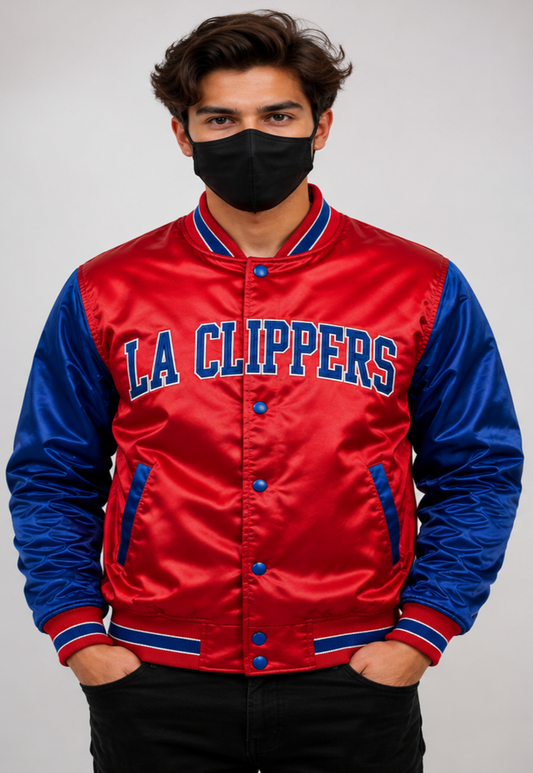 A man wearing a red and blue satin LA Clippers varsity jacket, a black face mask, and black pants, standing against a light gray studio background.