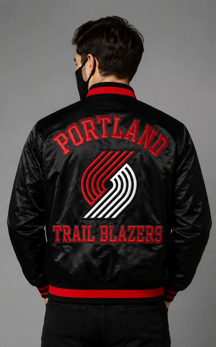 A man viewed from behind wearing a black satin bomber jacket with red and white embroidered 'PORTLAND TRAIL BLAZERS' text and logo on the back, against a plain gray studio background.
