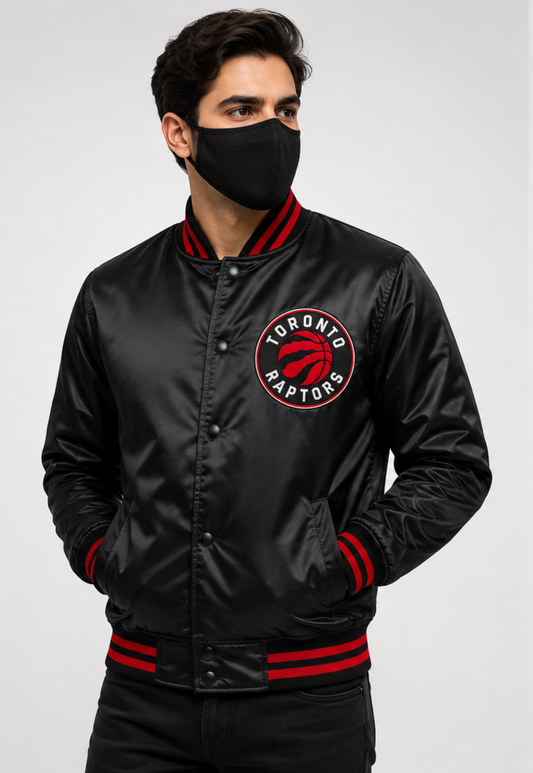 A man wearing a black satin bomber jacket with red and white ribbed trim and a Toronto Raptors logo on the chest, paired with a black face mask against a light gray background.