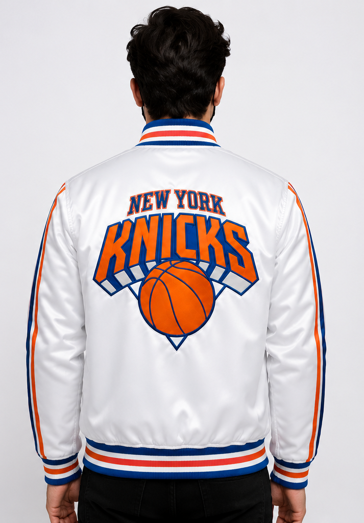 A man viewed from behind wearing a white satin New York Knicks bomber jacket with orange and blue trim and a large team logo on the back.