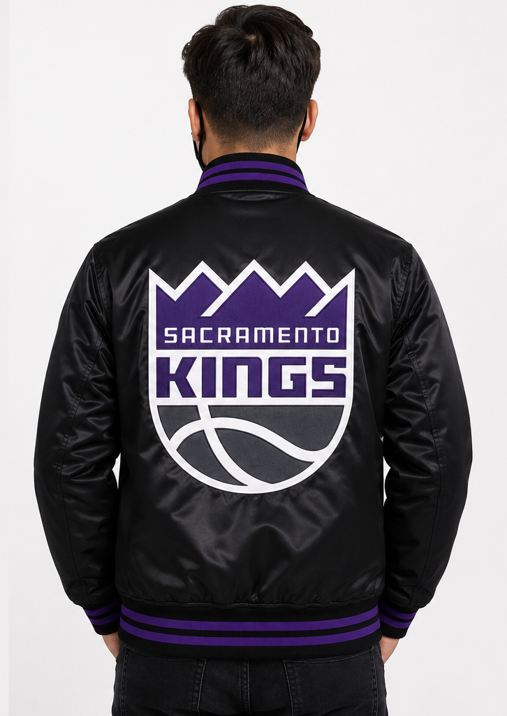 A man viewed from behind wearing a black satin bomber jacket with the Sacramento Kings logo in purple and white on the back, set against a plain light gray background.