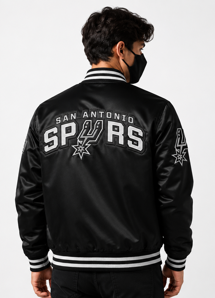 A man wearing a black San Antonio Spurs satin bomber jacket, viewed from the back. The jacket features white and black striped ribbed collar, cuffs, and hem, with 'SAN ANTONIO SPURS' and the team logo embroidered on the back.