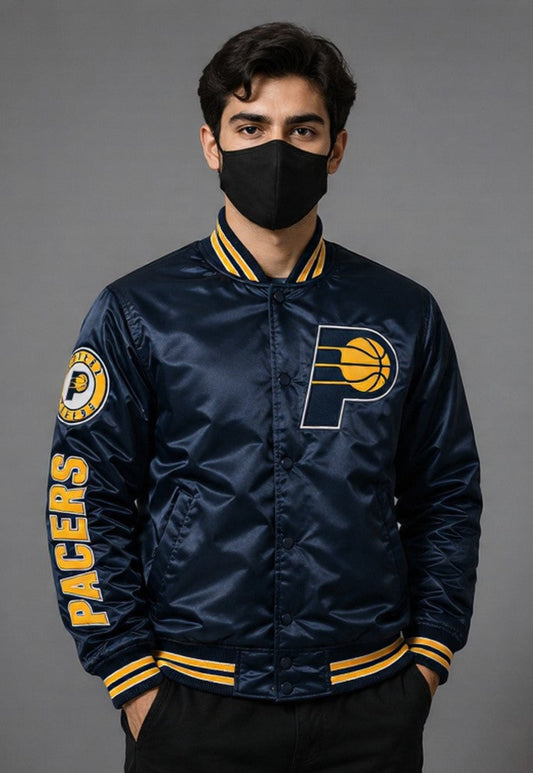 A man wearing a navy blue satin Indiana Pacers varsity jacket with yellow and white accents, a black face mask, and black pants, standing against a solid gray studio background.