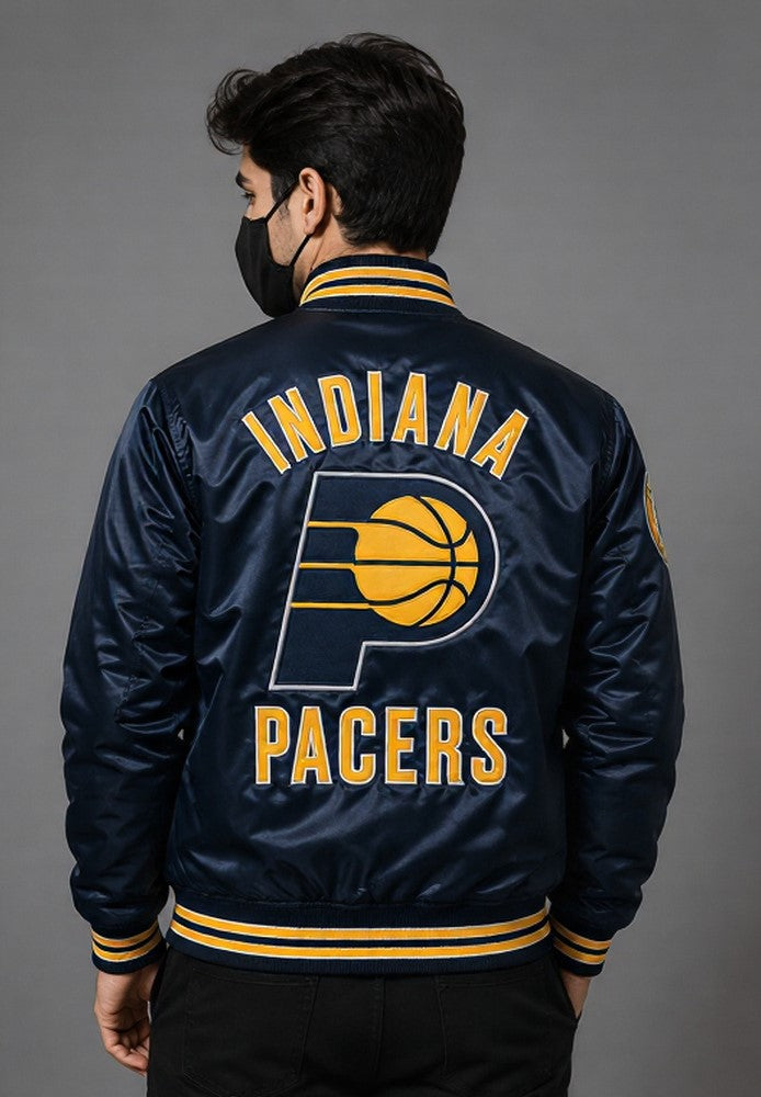 A man viewed from behind wearing a navy blue satin bomber jacket with 'INDIANA PACERS' and the embroidered team logo on the back, paired with a black face mask and black pants against a gray studio background