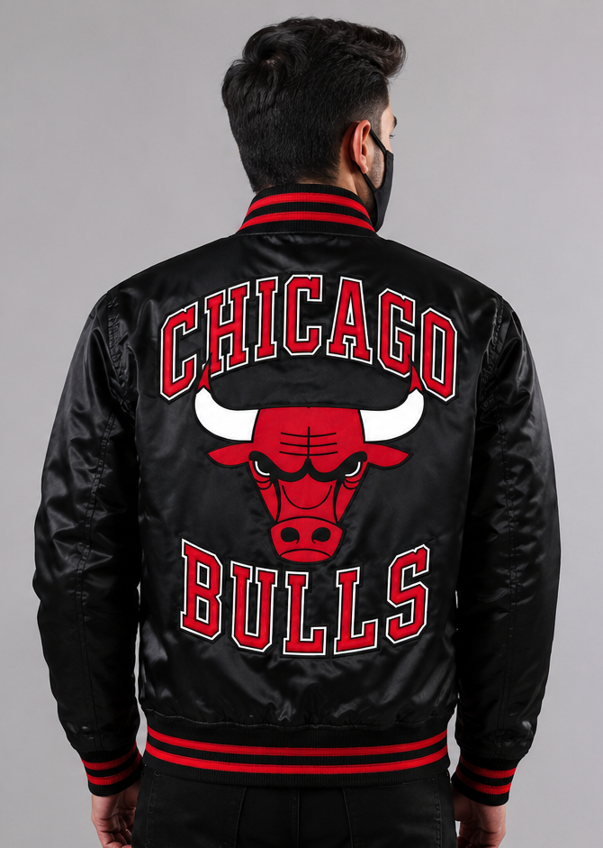 A man viewed from behind wearing a black Chicago Bulls satin jacket with red and white lettering and the team logo on the back, against a plain gray studio background.