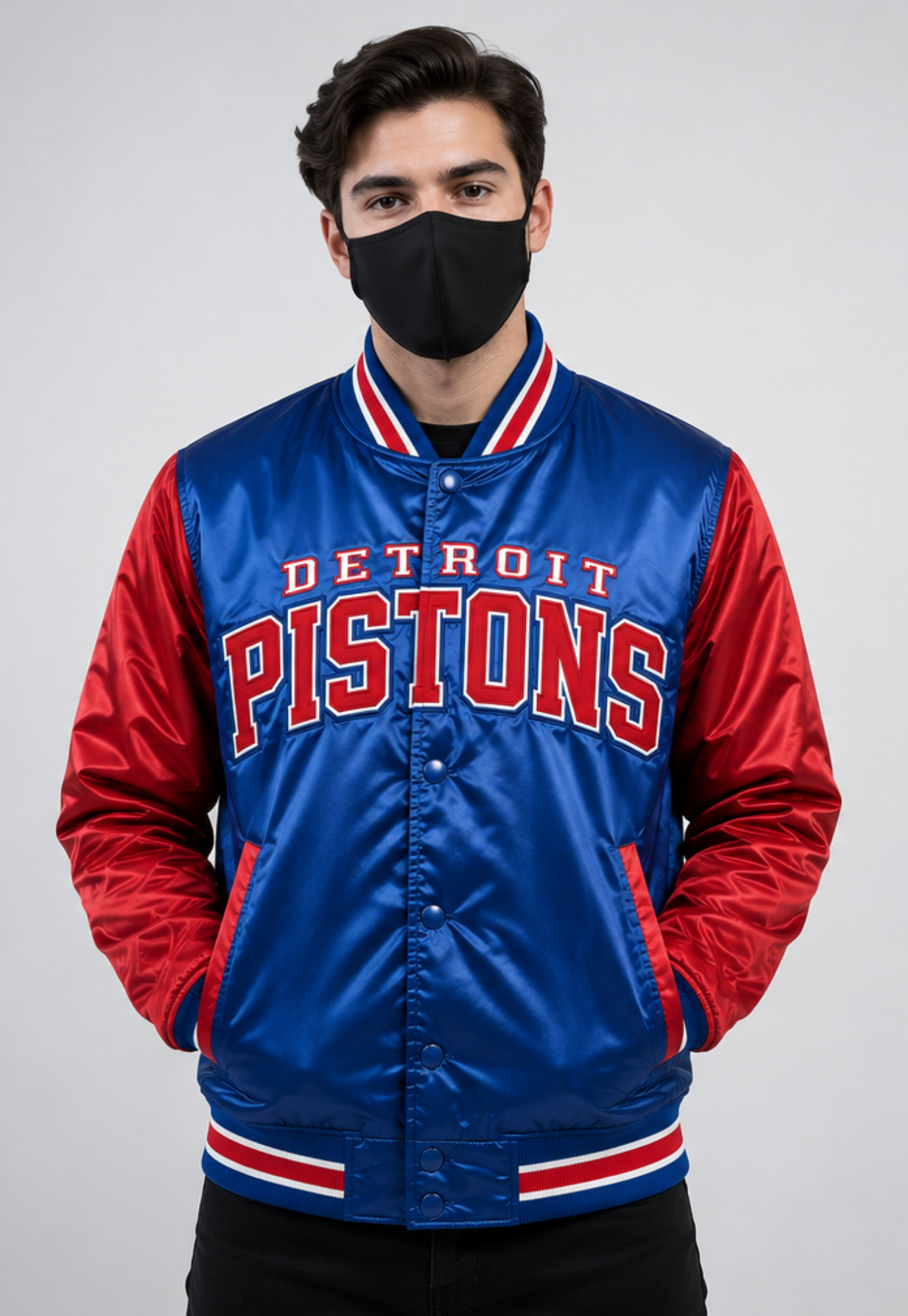 A man wearing a Detroit Pistons satin varsity jacket with red sleeves and a black face mask, photographed against a light gray studio background.