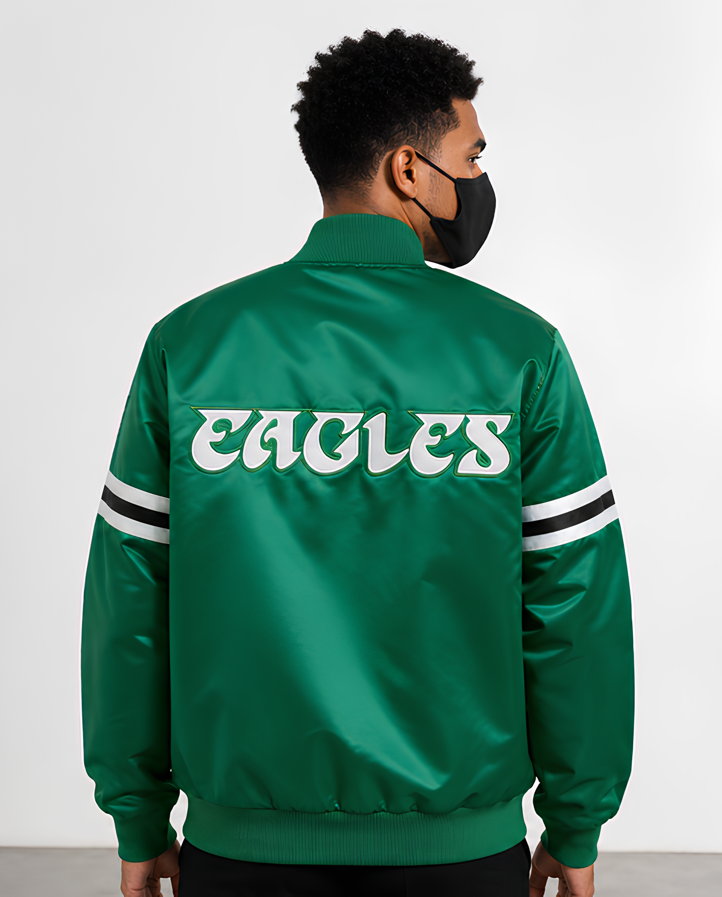 Person wearing a Philadelphia Eagles  green 'Eagles' jacket with white lettering on a plain background