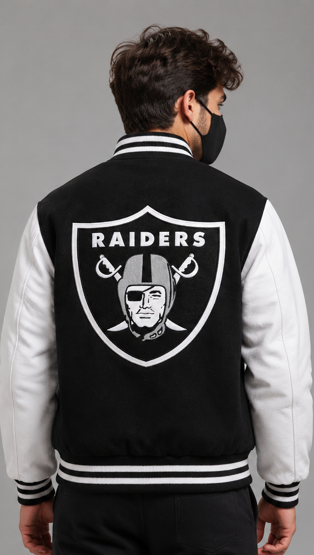 A man wearing a black and white Raiders varsity jacket, viewed from the back. The jacket features a large black and white Oakland Raiders shield logo on the back, with white sleeves and black-and-white striped ribbed collar, cuffs, and hem.