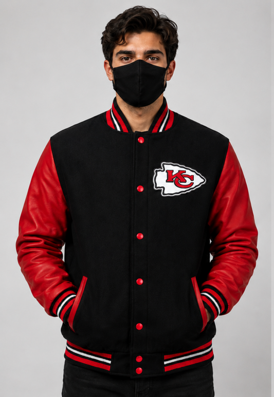 A man wearing a black and red Kansas City Chiefs varsity jacket with a black face mask, standing against a neutral gray background.