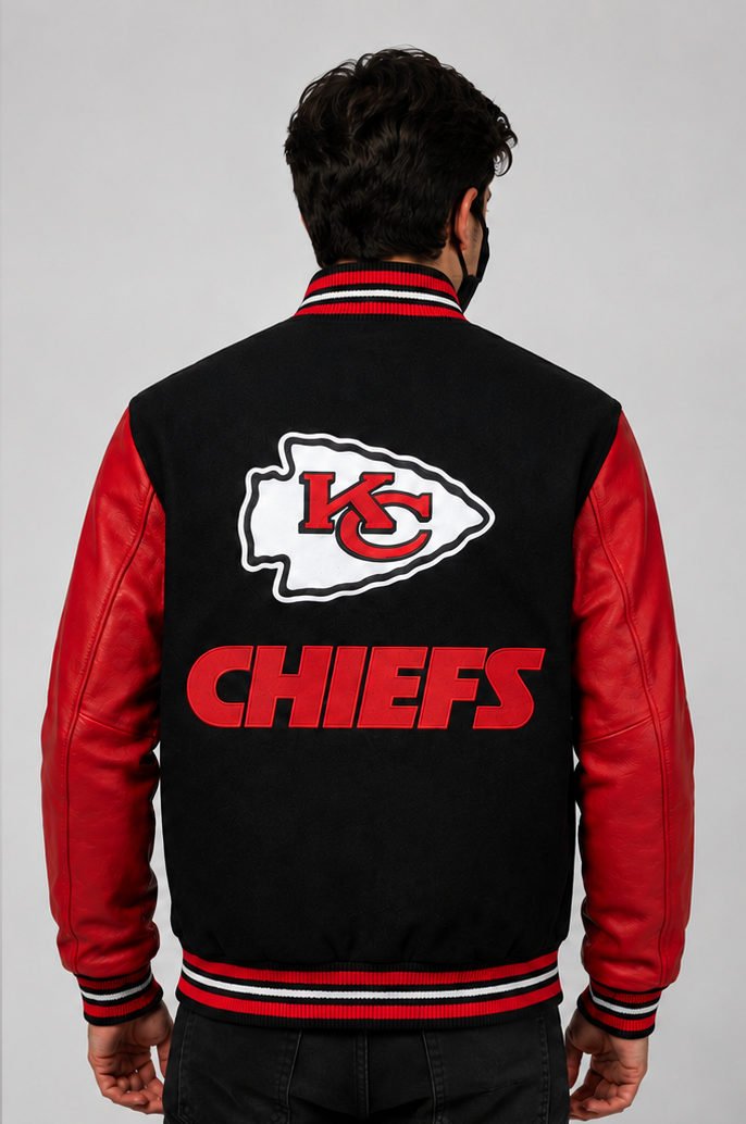 A man viewed from behind wearing a Kansas City Chiefs varsity jacket with a black body, red sleeves, and a large embroidered Chiefs logo and 'CHIEFS' text on the back.