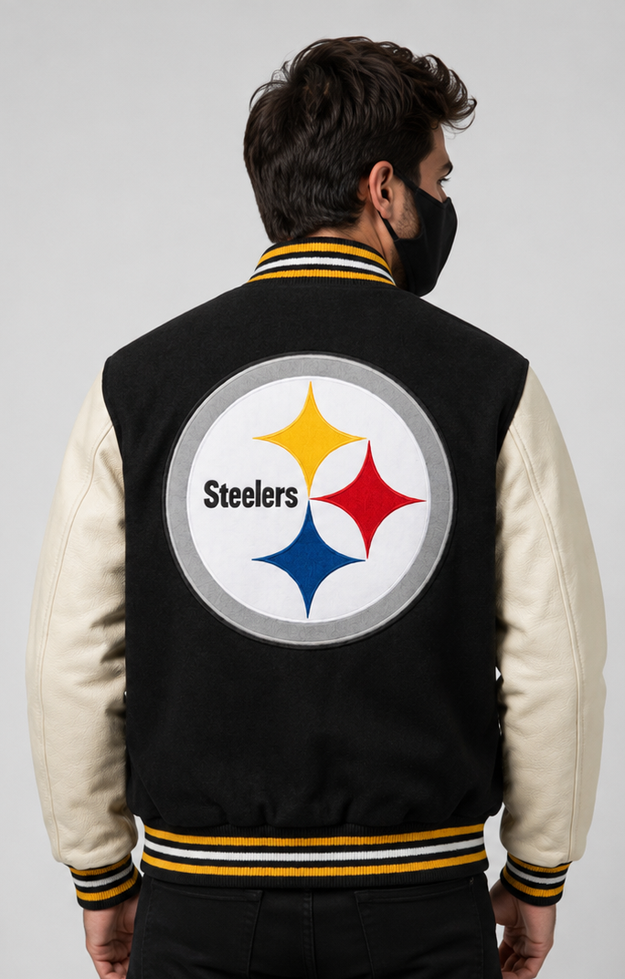 A man viewed from behind wearing a black and cream varsity jacket with the Pittsburgh Steelers embroidery logo on the back, set against a plain light gray studio background.