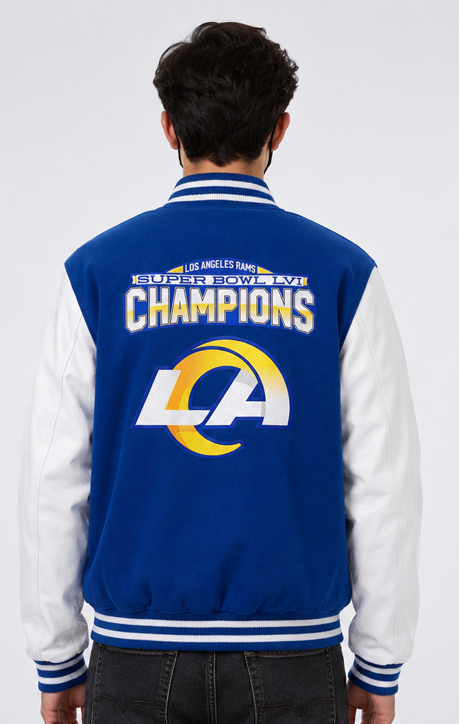 A man viewed from behind wearing a Los Angeles Rams varsity jacket with 'Champions' and the Super Bowl LV 1 embroidery logo on the back. The jacket has a royal blue body and white sleeves, with blue and white striped ribbed collar, cuffs, and hem.