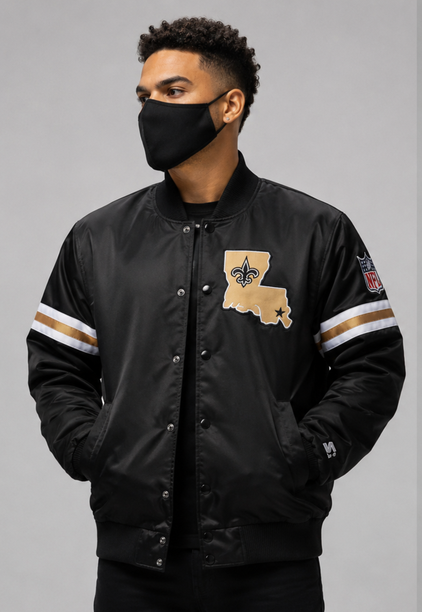 Person wearing a New Orleans Saints black jacket with a state design and patches on a gray background