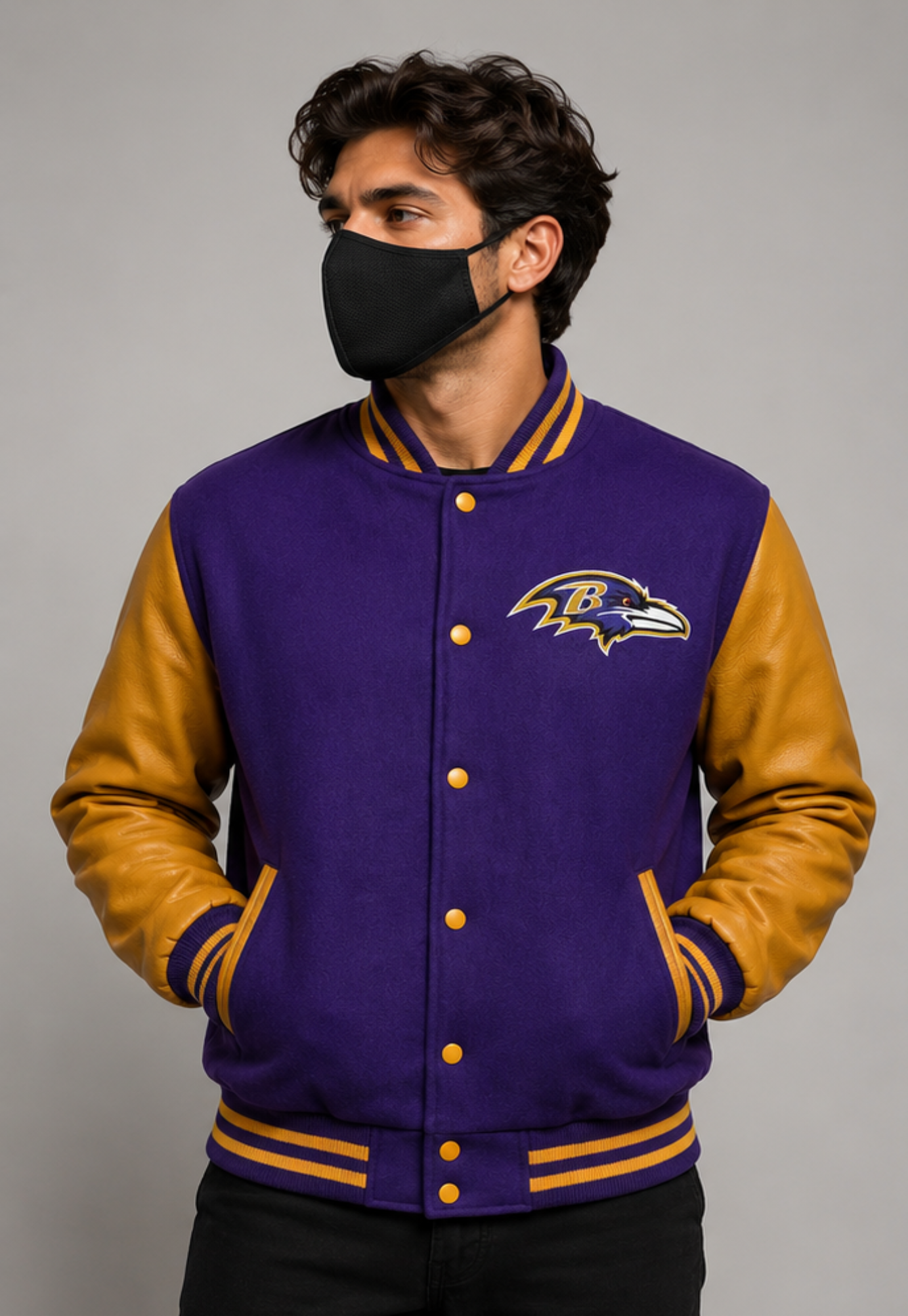A man wearing a purple and gold Baltimore Ravens varsity jacket, featuring a purple body, gold sleeves, and the team logo on the chest, photographed against a neutral gray background.