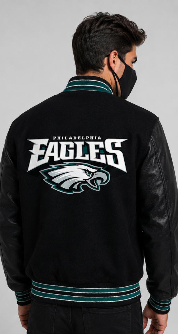 A man viewed from the back wearing a Philadelphia Eagles varsity jacket with black leather-look sleeves, teal and white striped ribbing, and a large white and teal eagle logo on the back.