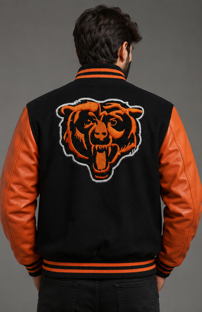 A man viewed from behind wearing a black and orange varsity jacket with a large embroidered Chicago Bears bear head on the back, set against a solid gray studio background.