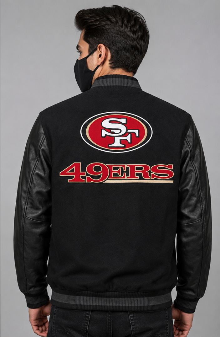 A man viewed from the back wearing a black San Francisco 49ers varsity-style jacket with black leather-look sleeves and a large red, white, and gold team logo on the back.