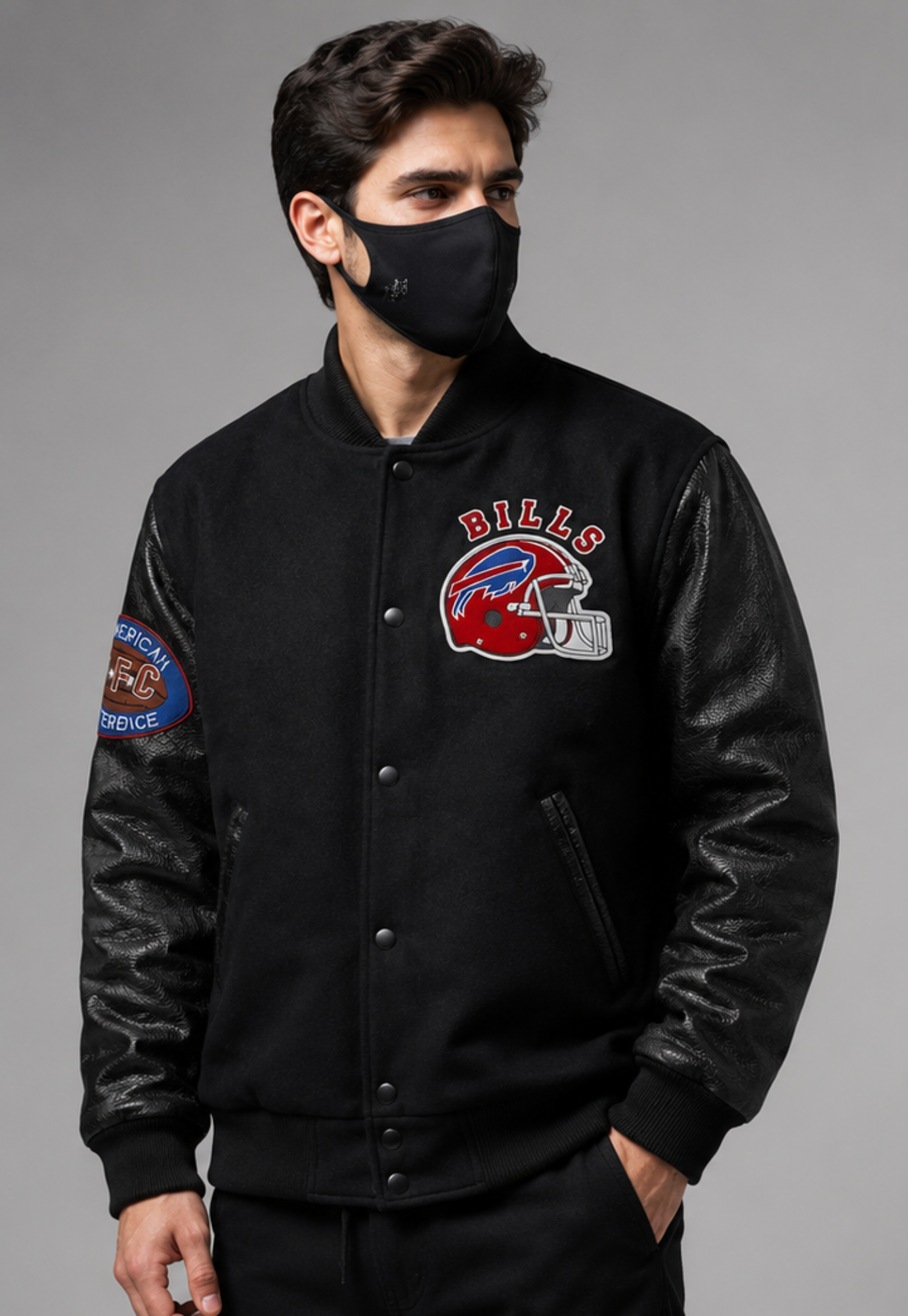 A man wearing a black varsity-style jacket with black leather sleeves, featuring a Buffalo Bills helmet patch on the left chest and a service patch on the right sleeve, posed against a solid gray background.