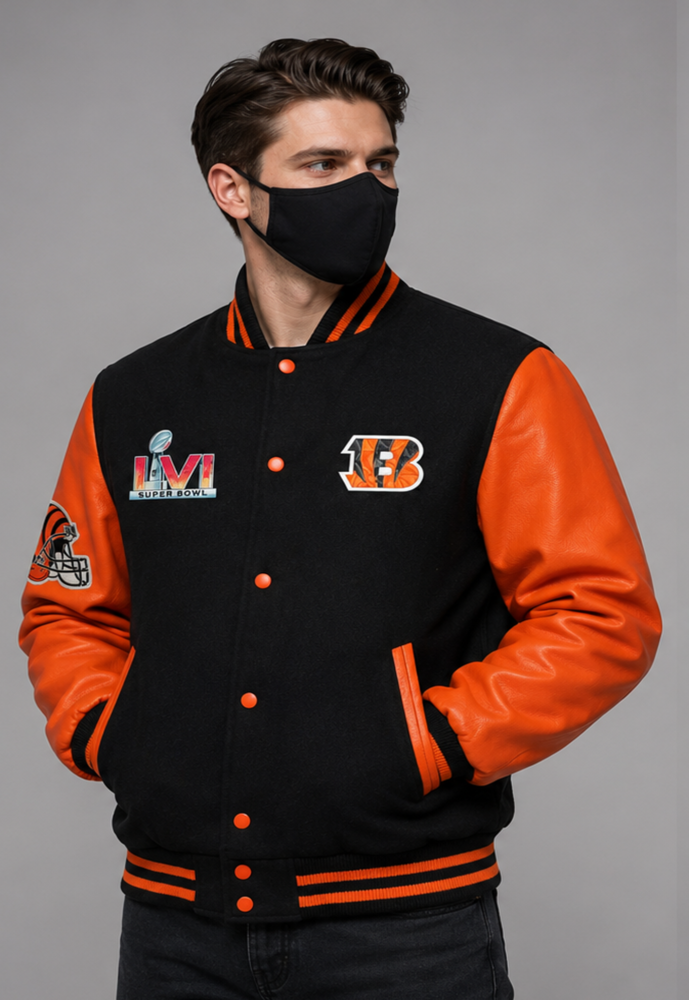 A man wearing a black and orange Cincinnati Bengals varsity jacket with a black face mask, posed against a solid gray studio background.
