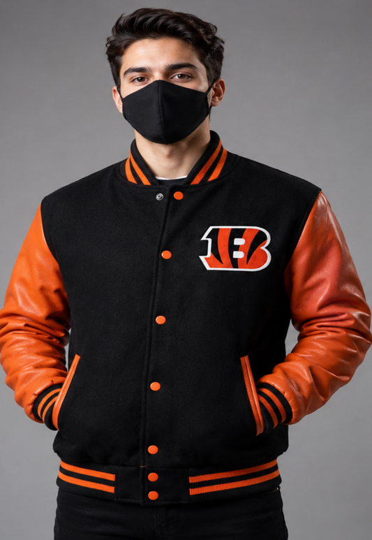 A man wearing a black and orange varsity jacket with the Cincinnati Bengals 'B' logo on the chest, paired with a black face mask, against a gray studio background.