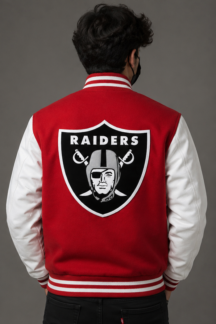 A man viewed from behind wearing a red and white varsity jacket with the Oakland Raiders logo on the back, set against a solid gray studio background.