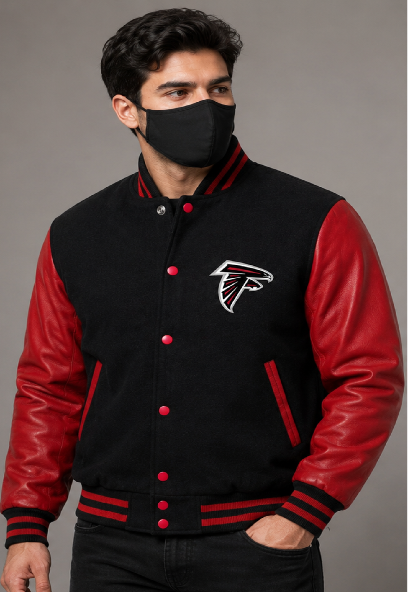 A man wearing a black and red varsity jacket with the Atlanta Falcons logo on the chest, paired with a black face mask, set against a plain gray studio background.
