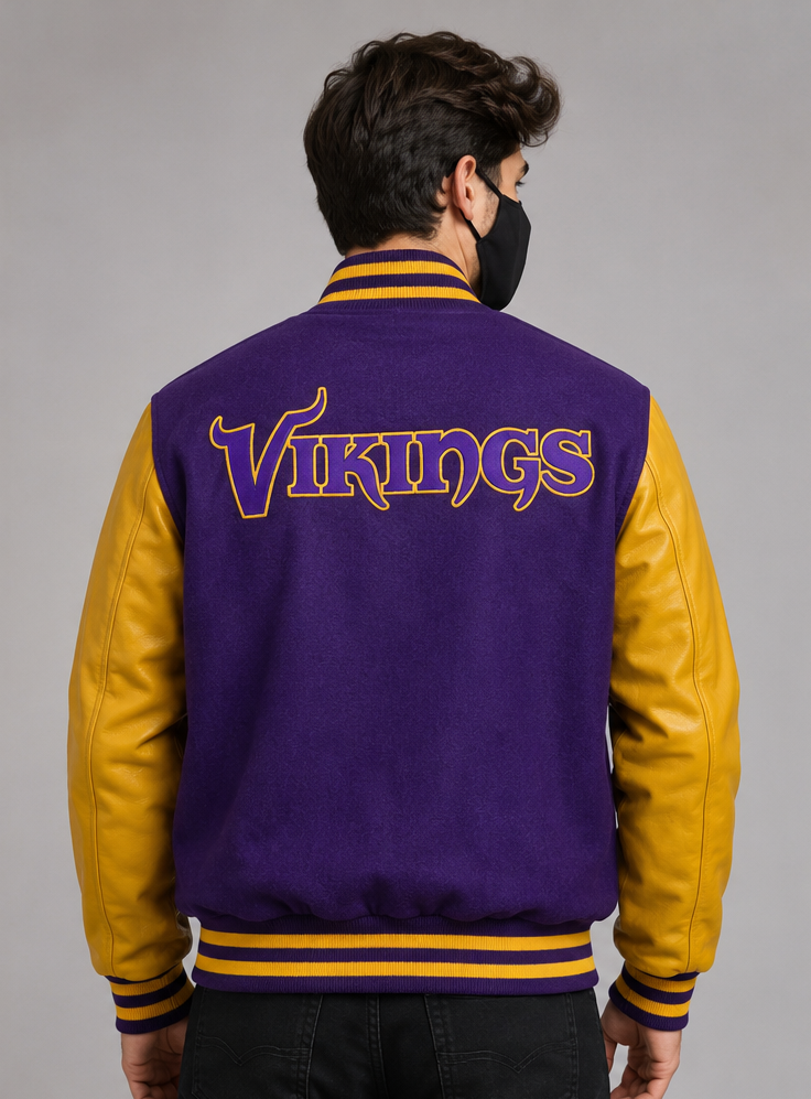 A man viewed from behind wearing a purple and gold varsity jacket with 'Vikings' embroidered across the back, set against a plain gray studio background.