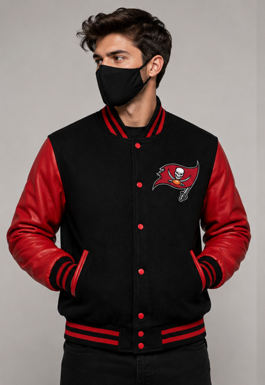 A man wearing a Tampa Bay Buccaneers varsity jacket with a black fleece body and red faux leather sleeves, paired with a black face mask, against a neutral gray background.