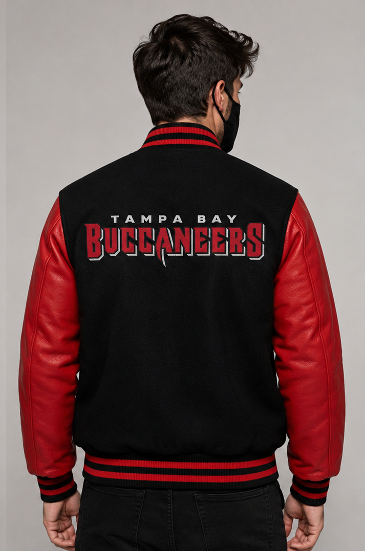 A man viewed from the back wearing a black and red varsity jacket with 'Tampa Bay Buccaneers' printed in red and white across the back, set against a plain gray studio background.