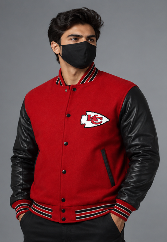 A man wearing a red and black Kansas City Chiefs varsity jacket with black leather sleeves, a black face mask, and black pants, posed against a solid gray studio background.