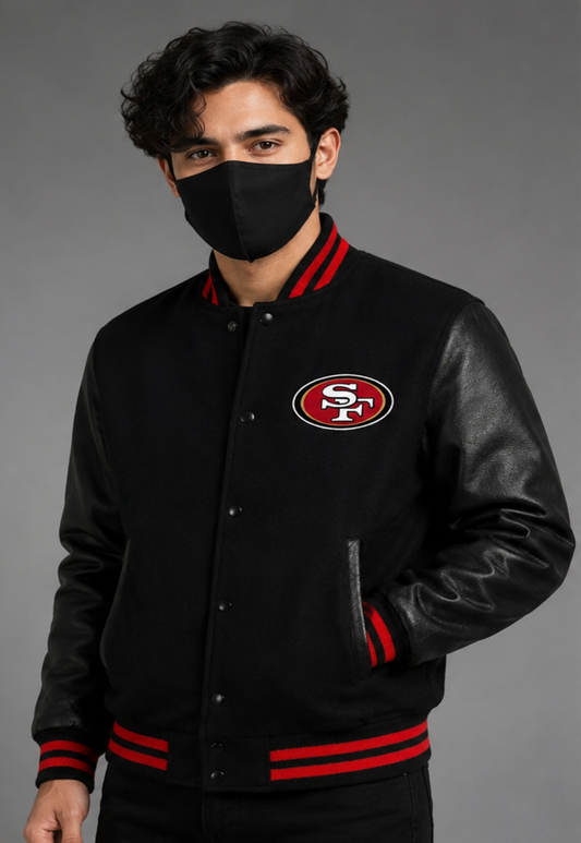 A man wearing a black varsity-style jacket with black leather sleeves, red and white striped ribbing, and a San Francisco 49ers logo on the chest, photographed against a gray studio background.