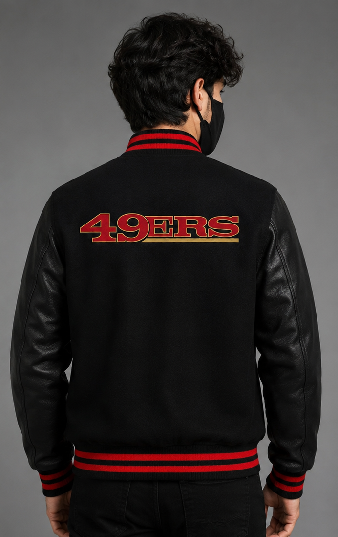 A man viewed from the back wearing a black varsity-style jacket with black leather sleeves, red and black striped ribbed trim, and a large red '49ERS' logo across the upper back.