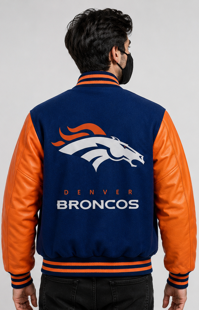 A man viewed from behind wearing a navy blue and orange Denver Broncos varsity jacket with the team logo and text on the back, set against a plain light gray background.